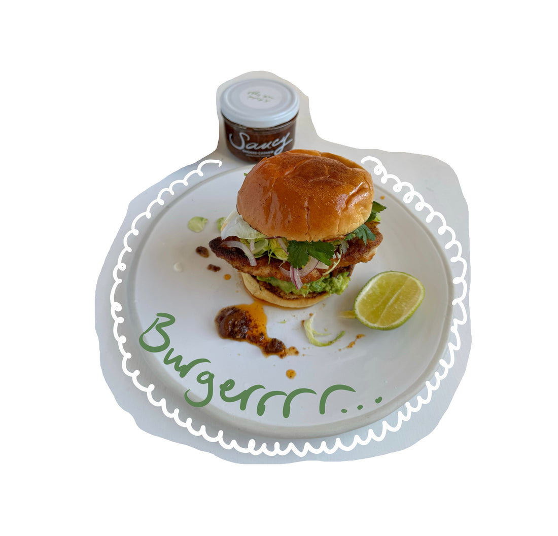Crispy chicken burger with lettuce, avocado, red onion and coriander on a toasted bun, served on a plate with lime